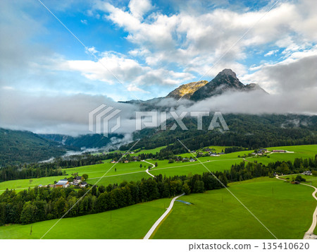 View of Austrian Alps landscape, mountain peak Sarstein in the morning mist and clouds. The meadow in foreground. 135410620