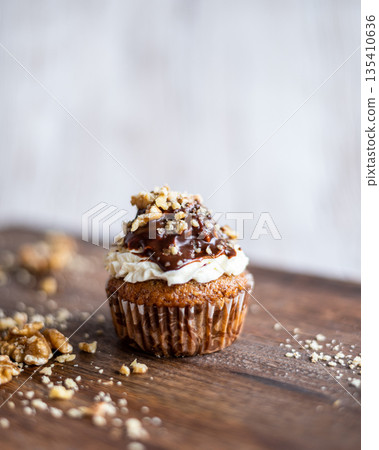 Tasty chocolate muffin with creme mascarpone and chocolate on top, covered with nuts. Placed on wooden desk. Sweet fresh and homemade cupcake. Tasty chocolate muffin with creme mascarpone and chocolate on top, covered with nuts. Placed on wooden desk. Sweet fresh and homemade cupcake. 135410636