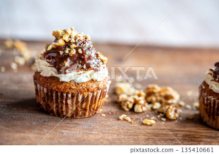 Tasty chocolate muffin with creme mascarpone and chocolate on top, covered with nuts. Placed on wooden desk. Sweet fresh and homemade cupcake. Tasty chocolate muffin with creme mascarpone and chocolate on top, covered with nuts. Placed on wooden desk. Sweet fresh and homemade cupcake. 135410661