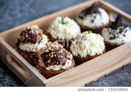 Cupcakes and muffins placed in wooden box. Chocolate and creme with nuts. Fresh home make baked sweets. Cupcakes and muffins placed in wooden box. Chocolate and creme with nuts. Fresh home make baked sweets. 135410663