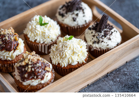 Cupcakes and muffins placed in wooden box. Chocolate and creme with nuts. Fresh home make baked sweets. Cupcakes and muffins placed in wooden box. Chocolate and creme with nuts. Fresh home make baked sweets. 135410664
