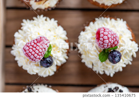 Tasty sweet muffins with mascarpone creme and chocolate, raspberry and blueberry. Fresh home baked sweets with fruit. Placed in wooden box. 135410675