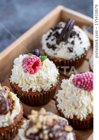 Tasty sweet muffins with mascarpone creme and chocolate, raspberry and blueberry. Fresh home baked sweets with fruit. Placed in wooden box. Tasty sweet muffins with mascarpone creme and chocolate, raspberry and blueberry. Fresh home baked sweets with fruit. Placed in wooden box. 135410679