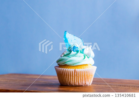 Homemade cupcake of blue color placed on wooden desk. Winter and christmas theme, snowflakes on cream with blue ice. Fresh and home baked sweet. 135410681