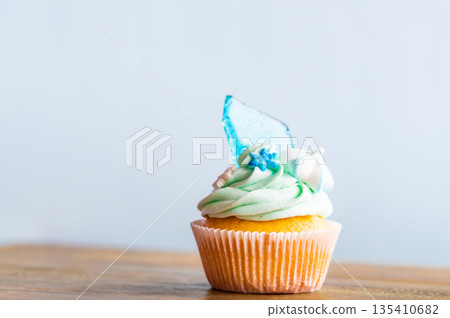 Homemade cupcake of blue color placed on wooden desk. Winter and christmas theme, snowflakes on cream with blue ice. Fresh and home baked sweet. Homemade cupcake of blue color placed on wooden desk. Winter and christmas theme, snowflakes on cream with blue ice. Fresh and home baked sweet. 135410682
