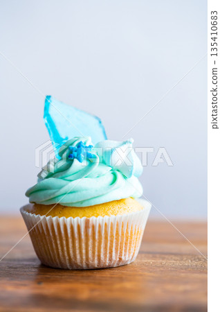 Homemade cupcake of blue color placed on wooden desk. Winter and christmas theme, snowflakes on cream with blue ice. Fresh and home baked sweet. Homemade cupcake of blue color placed on wooden desk. Winter and christmas theme, snowflakes on cream with blue ice. Fresh and home baked sweet. 135410683