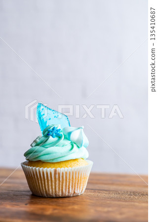 Homemade cupcake of blue color placed on wooden desk. Winter and christmas theme, snowflakes on cream with blue ice. Fresh and home baked sweet. Homemade cupcake of blue color placed on wooden desk. Winter and christmas theme, snowflakes on cream with blue ice. Fresh and home baked sweet. 135410687