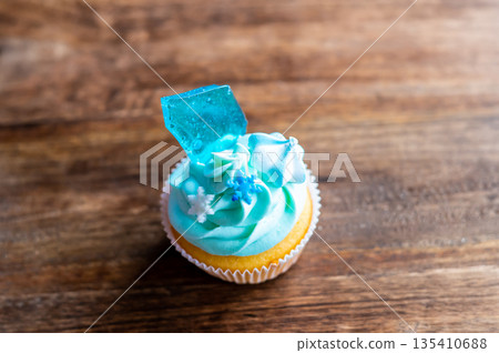 Homemade cupcake of blue color placed on wooden desk. Winter and christmas theme, snowflakes on cream with blue ice. Fresh and home baked sweet. Homemade cupcake of blue color placed on wooden desk. Winter and christmas theme, snowflakes on cream with blue ice. Fresh and home baked sweet. 135410688