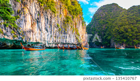 View of long tail boats on turquoise water at ocean near Ko Phi Phi islands, Thailand. Concept of exotic vacation in tropical paradise. Limestone rock in background. 135410767
