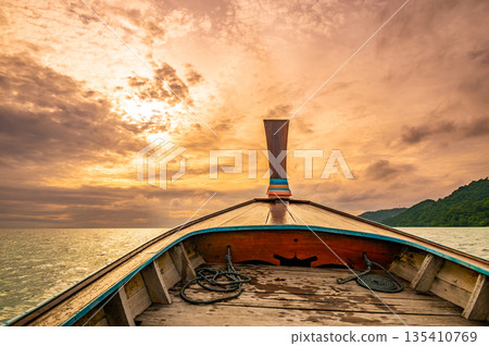 View from long tail boat heading to the dramatic sunset above ocean. Concept of exotic vacation in tropical paradise. Photo taken at Thailand near Ko Phi Phi islands. View from long tail boat heading to the dramatic sunset above ocean. Concept of exotic vacation in tropical paradise. Photo taken at Thailand near Ko Phi Phi islands. 135410769