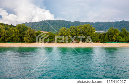 Aerial drone view of Koh Lanta island - the long beach. Famous tropical beach with white sand and turquoise ocean. The island mountains in background. Aerial drone view of Koh Lanta island - the long beach. Famous tropical beach with white sand and turquoise ocean. The island mountains in background. 135410917