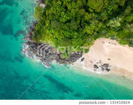 Aerial top down view of tropical beach with turquoise water, white sand and big rock. Trees and palms growing on the rock. Tropical theme. 135410924