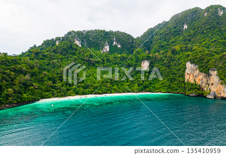 Aerial drone view of famous Monkey Beach at Ko Phi Phi island, Thailand. Tropical beach with white sand, turquoise water and green forest. Long tailed boats are waiting on beach. Exotic tourist 135410959