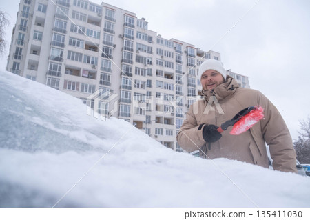 Man Clearing Snow from Car in Winter Cityscape 135411030