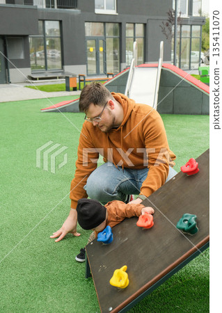 Father Assisting Toddler on Playground Climbing Wall 135411070