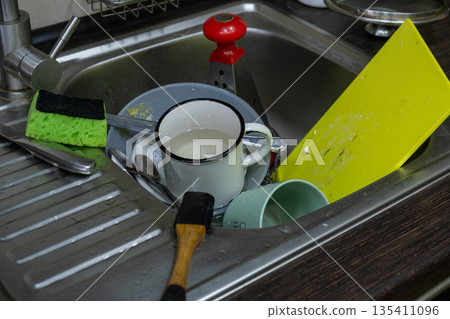 Cluttered kitchen sink with dirty dishes and sponges Cluttered kitchen sink with dirty dishes and sponges 135411096