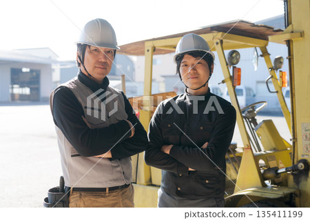 Two workers standing in front of a forklift Two workers standing in front of a forklift 135411199