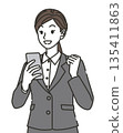 A woman in a suit who is pleased to see her smartphone 135411863