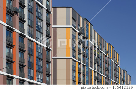 Modern residential building facade with colorful vertical panels in orange, yellow, beige, and blue Modern residential building facade with colorful vertical panels in orange, yellow, beige, and blue 135412159