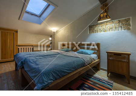 Rustic attic bedroom with twin beds and evening lighting Rustic attic bedroom with twin beds and evening lighting 135412485