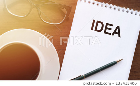 IDEA - text on paper with cup of coffee and glasses on wooden background in sinlight. IDEA - text on paper with cup of coffee and glasses on wooden background in sinlight. 135413400