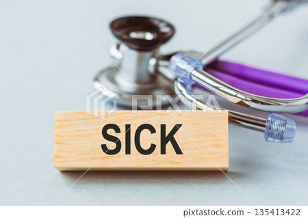 A stethoscope rests next to a sign that says sick on wooden cubes, symbolizing a medical concept related to illness. 135413422