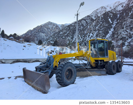 Yellow road grader parked in snow. Heavy machinery for snow removal 135413603