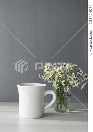 White mug and matricaria on a gray background. Copy space White mug and matricaria on a gray background. Copy space 135414083