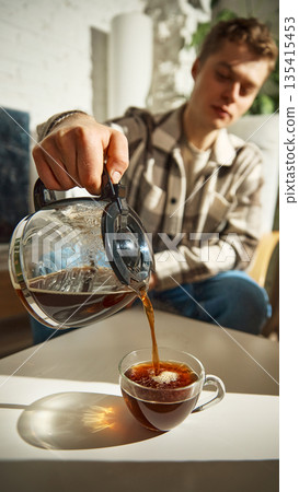 Coffee being poured from glass pot into transparent cup on table. Coffee being poured from glass pot into transparent cup on table. 135415453