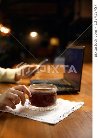 Coffee cup close up on table with laptop blurred in background. 135415457