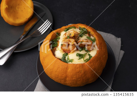 Whole baked pumpkin with tiger prawns, melted cheese and tomatoes. Traditional dish of Brazil, home cooking. Selective focus, close-up, black background. 135415635