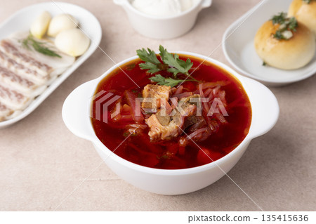 Borsch with pampushki (buns), sour cream, lard and garlic. Traditional Russian and Ukrainian soup with meat, beets, cabbage and potatoes. Close-up, selective focus. Borsch with pampushki (buns), sour cream, lard and garlic. Traditional Russian and Ukrainian soup with meat, beets, cabbage and potatoes. Close-up, selective focus. 135415636