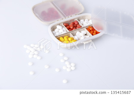 Pill box with colorful pills and vitamins. Plastic beige container with cells for medicines. Health concept. Selective focus, close-up. Pill box with colorful pills and vitamins. Plastic beige container with cells for medicines. Health concept. Selective focus, close-up. 135415687