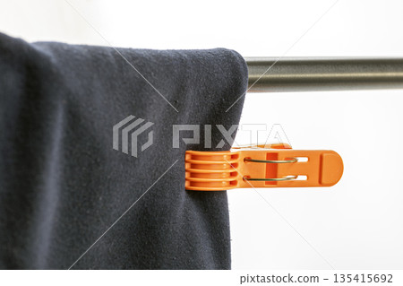 A close-up view of an orange plastic clothespin securing dark blue fabric to a shiny metal rod, part of a clothes drying rack. 135415692
