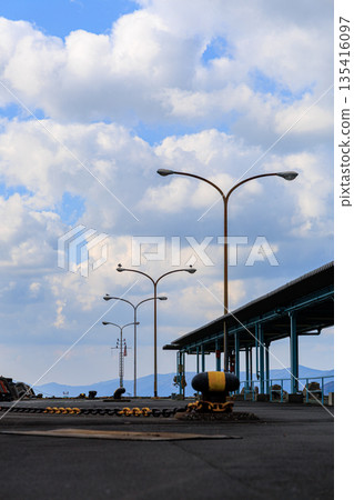 愛媛縣八幡濱港碼頭的廣角鏡頭。路燈和藍天。空曠的港口景色,遠處是連綿的山脈。 愛媛縣八幡濱港碼頭的廣角鏡頭。路燈和藍天。空曠的港口景色,遠處是連綿的山脈。 135416097