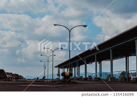 Wide-angle pier of Yawatahama Port, Ehime Prefecture. Street lights and blue sky. Empty harbor scenery with mountains in the distance. Wide-angle pier of Yawatahama Port, Ehime Prefecture. Street lights and blue sky. Empty harbor scenery with mountains in the distance. 135416099