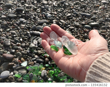 Woman put glass sea pebbles of different colours on shore, beach. Nature and ecology. Background for design. 135416132