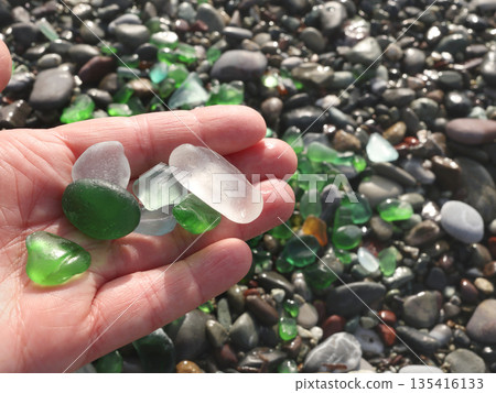 Woman put glass sea pebbles of different colours on shore, beach. Nature and ecology. Background for design. 135416133