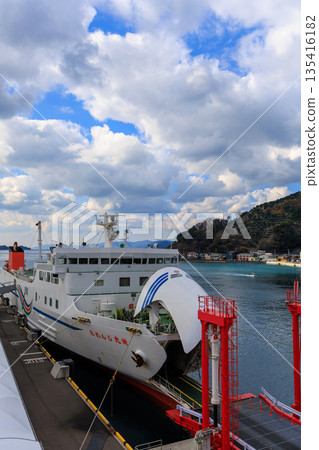Uwajima Nanyo Nada Ferry at Yawatahama Port in Ehime Prefecture. A white passenger ship is moored with a red loader. A harbor shipping scene with Mt. Momiji in the background. 135416182