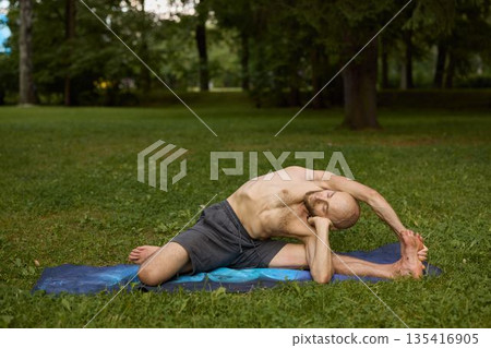 Person executing side bend exercise on blue mat under sunlight in park 135416905