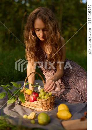 Woman setting fruit basket outdoors during golden light 135416922