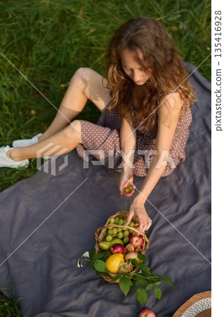 Woman selects orchard produce amidst sunny greenery Woman selects orchard produce amidst sunny greenery 135416928