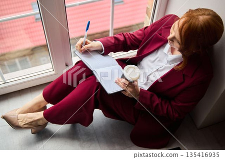 Woman concentrating on presentation while enjoying coffee by window 135416935