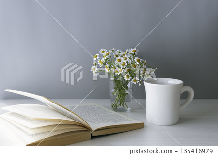白色馬克杯，上面印有母本圖案和一本打開的書。灰色背景，留有文字空間。 135416979