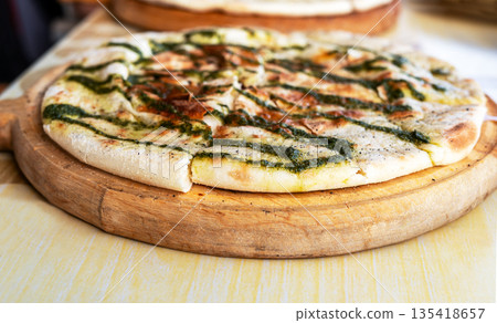 side view of thin focaccia flatbread sliced on wooden board and drizzled with green pesto sauce, Mediterranean cuisine and bakery Traditional Italian bread with crispy crust, served on rustic table side view of thin focaccia flatbread sliced on wooden board and drizzled with green pesto sauce, Mediterranean cuisine and bakery Traditional Italian bread with crispy crust, served on rustic table 135418657