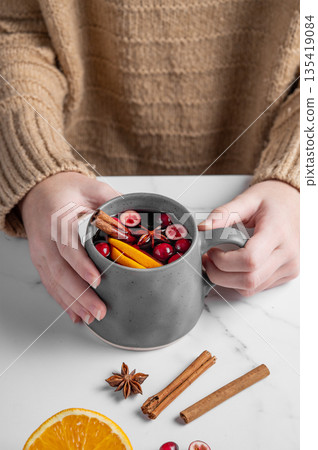 A woman in a beige sweater holds a mug of non-alcoholic mulled wine or a spicy hot drink A woman in a beige sweater holds a mug of non-alcoholic mulled wine or a spicy hot drink 135419084