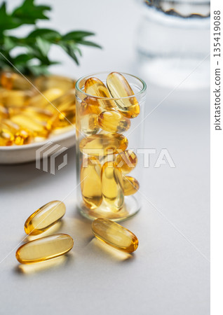 Yellow softgel vitamins capsules scattered in a bottle on a light isolated background with  branch. 135419088