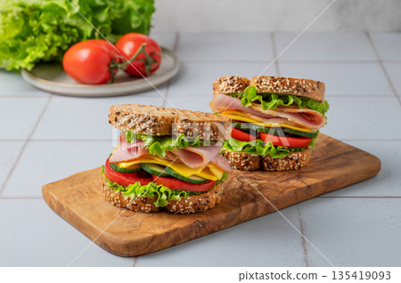 Two sandwich or toasts with ham, cheese, lettuce and vegetables on a wooden board 135419093