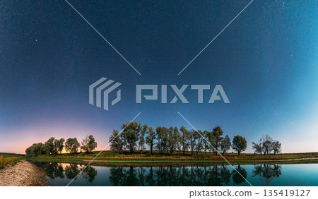 Night Starry Sky Above Lake River. Night Glowing Stars And Trees Woods Reflected In Water. Night Landscape. Panorama 135419127