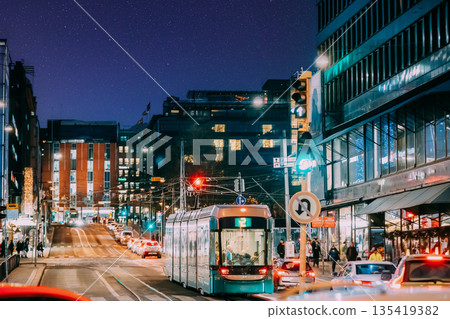 Helsinki, Finland. Tram Departs From A Stop On Kaivokatu Street In Helsinki. Night View Of Kaivokatu Street In Kluuvi District In Evening Or Night Illumination. Starry sky above scene. Night stars Helsinki, Finland. Tram Departs From A Stop On Kaivokatu Street In Helsinki. Night View Of Kaivokatu Street In Kluuvi District In Evening Or Night Illumination. Starry sky above scene. Night stars 135419382
